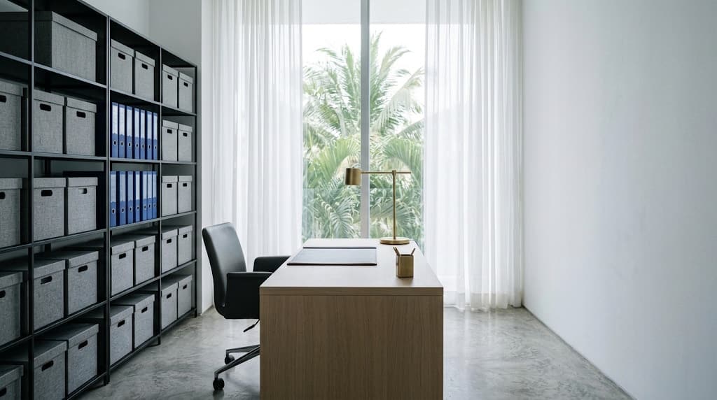 Libreros de archivo, carpetas azules y un escritorio de madera junto a una ventana con palmeras.